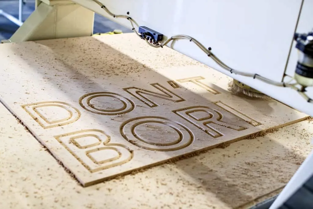 "Don't Be Boring" Choura mantra being engraved in wood by machine
